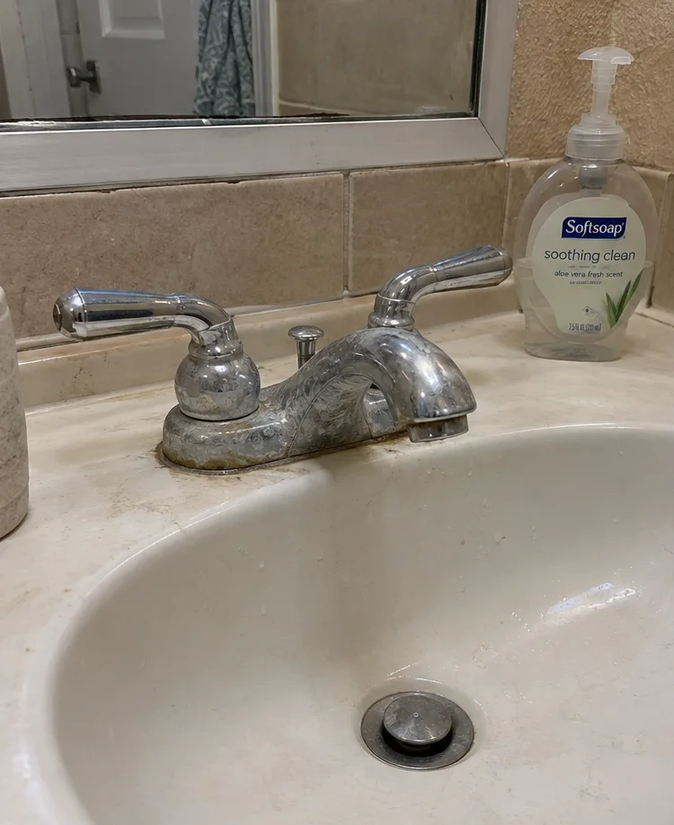 a scale-crusted, corroded chrome bathroom faucet on a beige sink