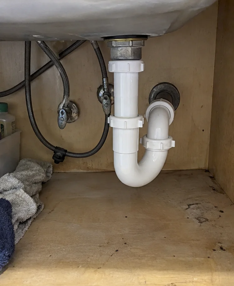 a new white PVC P-trap under the same sink, cabinet floor dry