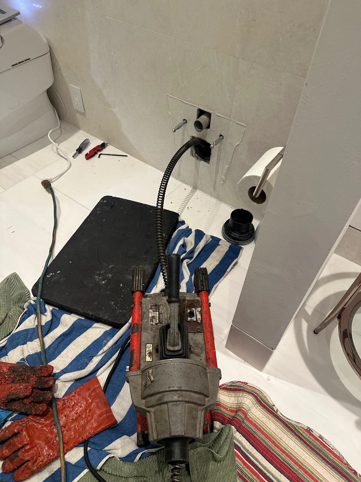 A drain machine and cable set up on drop cloths in a bathroom, ready to clear a line