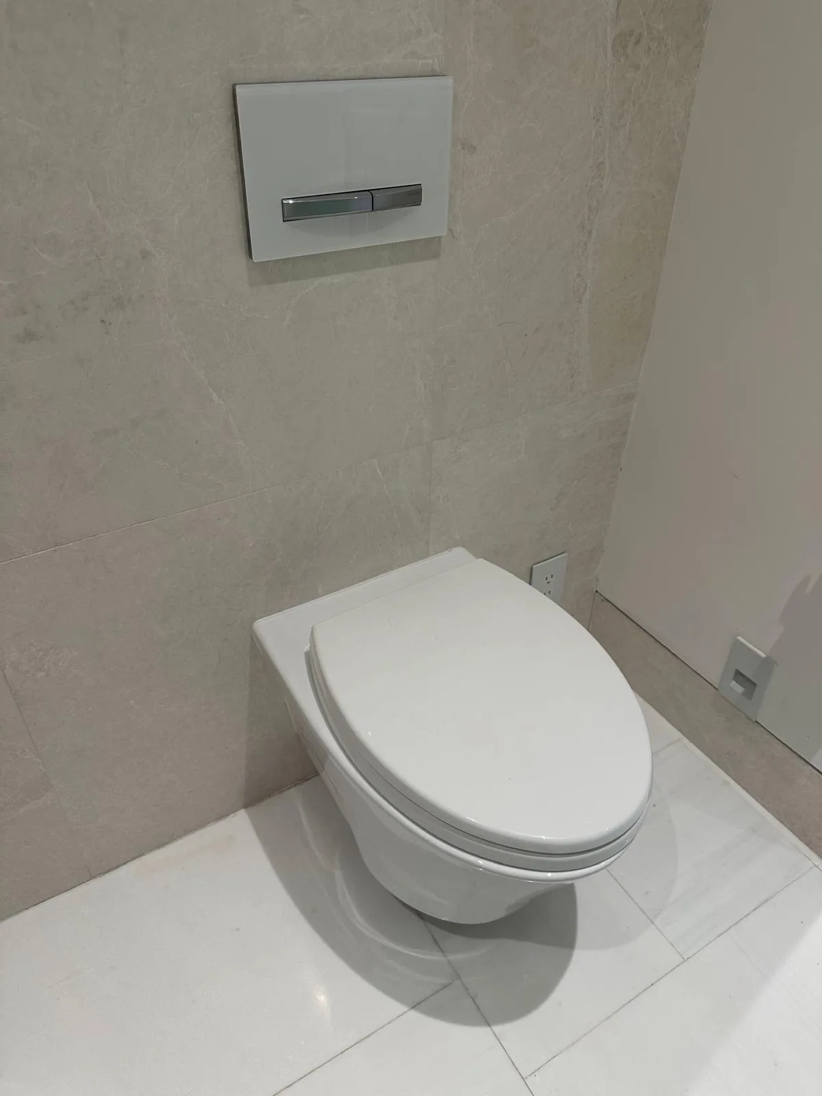 A wall-hung toilet with a concealed tank and flush plate in a tiled bathroom