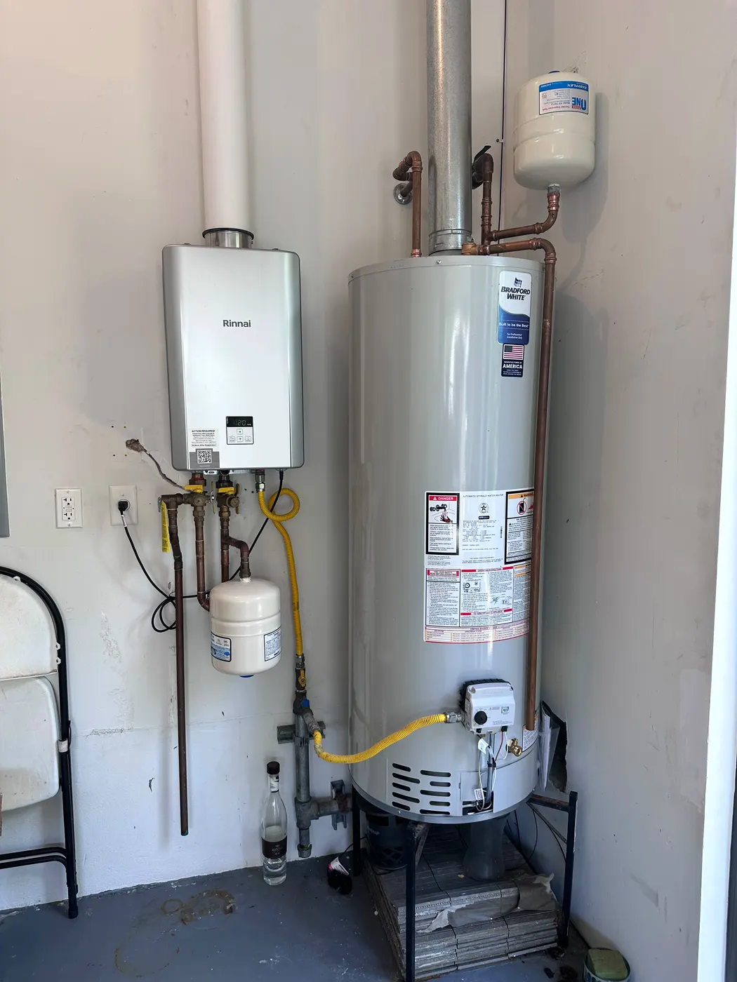 A new gas tank water heater and a wall-mounted tankless unit installed side by side in a garage